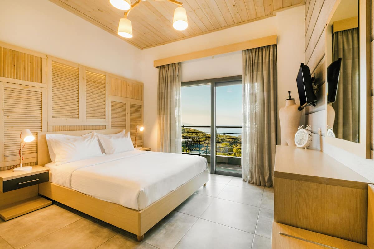 A bedroom with a large bed, bedside tables, a dresser, a mirror, and a view of the outdoors.