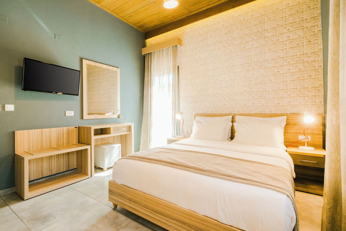 A modern bedroom with a wooden bed, a flat-screen TV, a bedside table with a lamp, and a built-in wooden shelf.