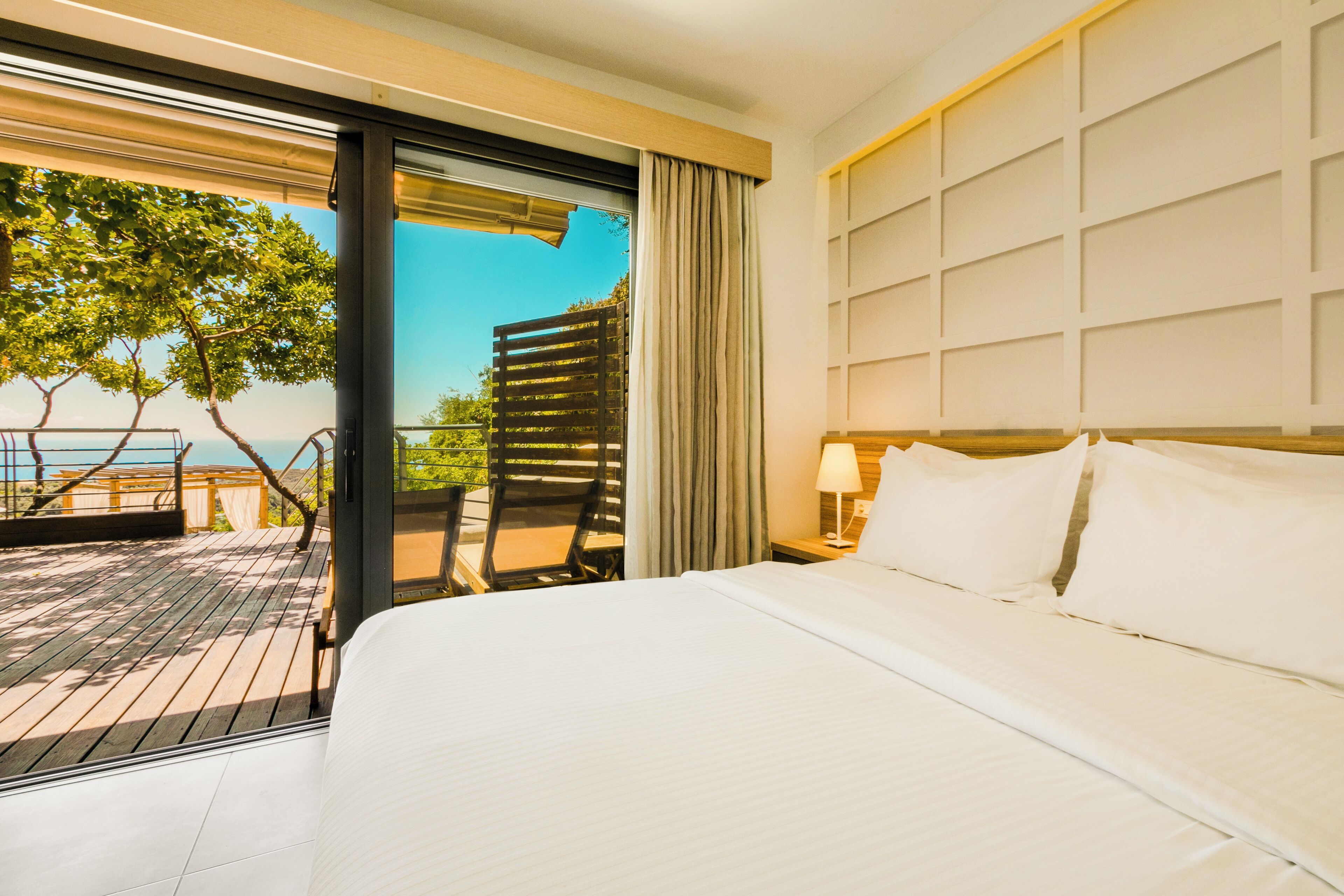 A hotel room with a large bed, a view of the ocean, and a balcony with outdoor furniture.