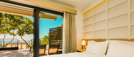 A hotel room with a large bed, a view of the ocean, and a balcony with outdoor furniture.