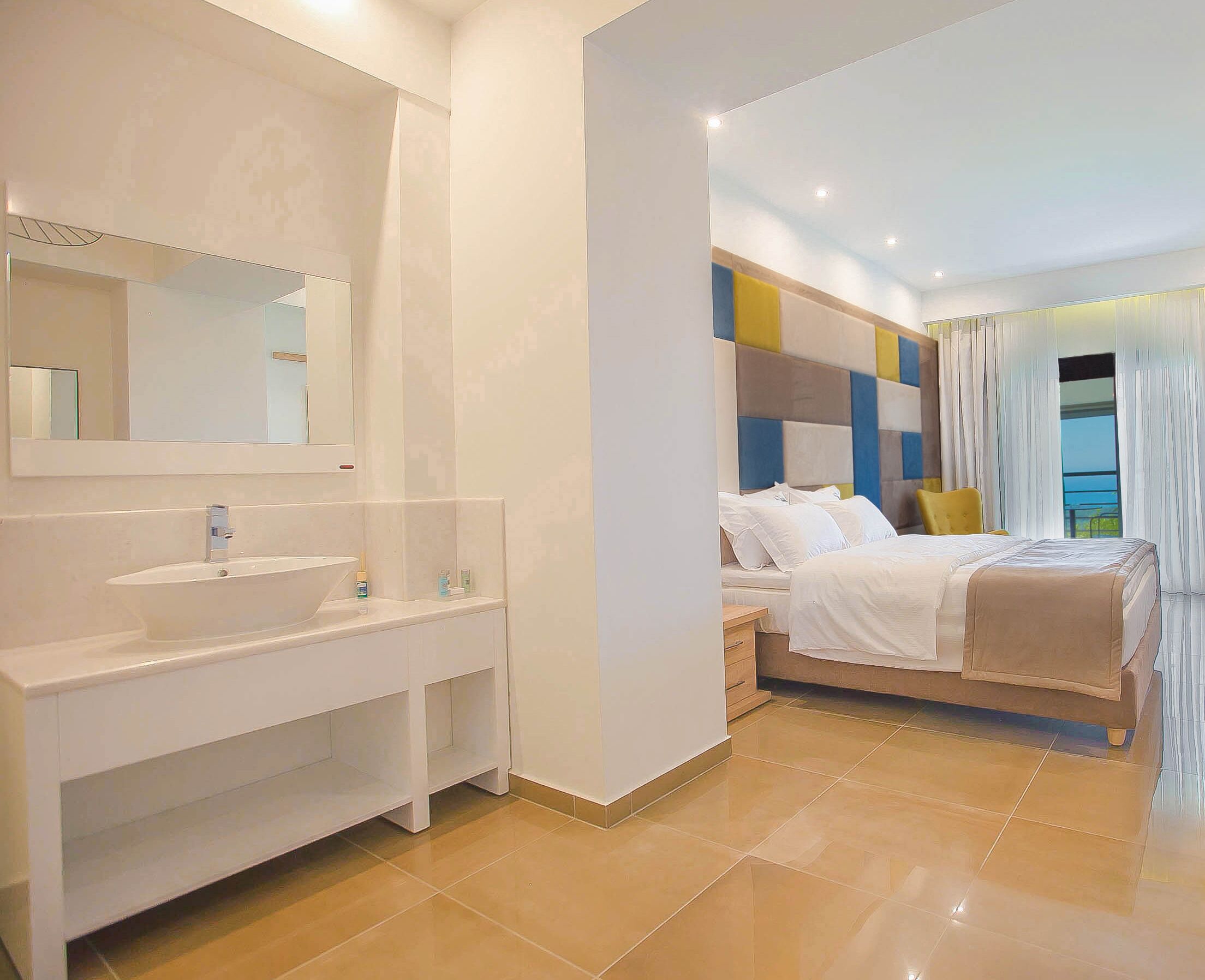 Una camera d'albergo moderna con un ampio mobile bagno, un letto con biancheria bianca e vista sull'esterno.