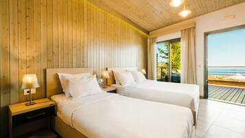 A hotel room with two beds, wooden paneling on the walls, and a balcony with a view of the sea.