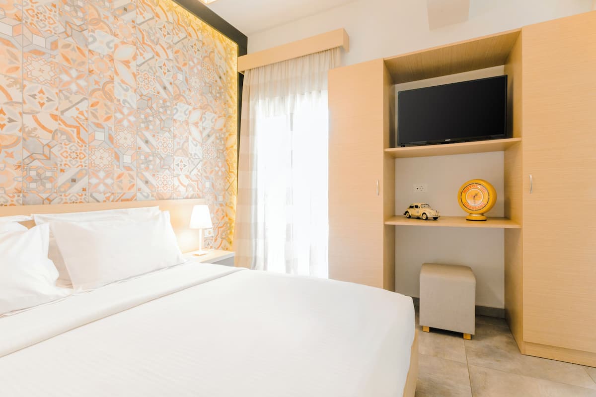 A hotel room with a large bed, a television on a shelf, a small table with a lamp, and a decorative wall.