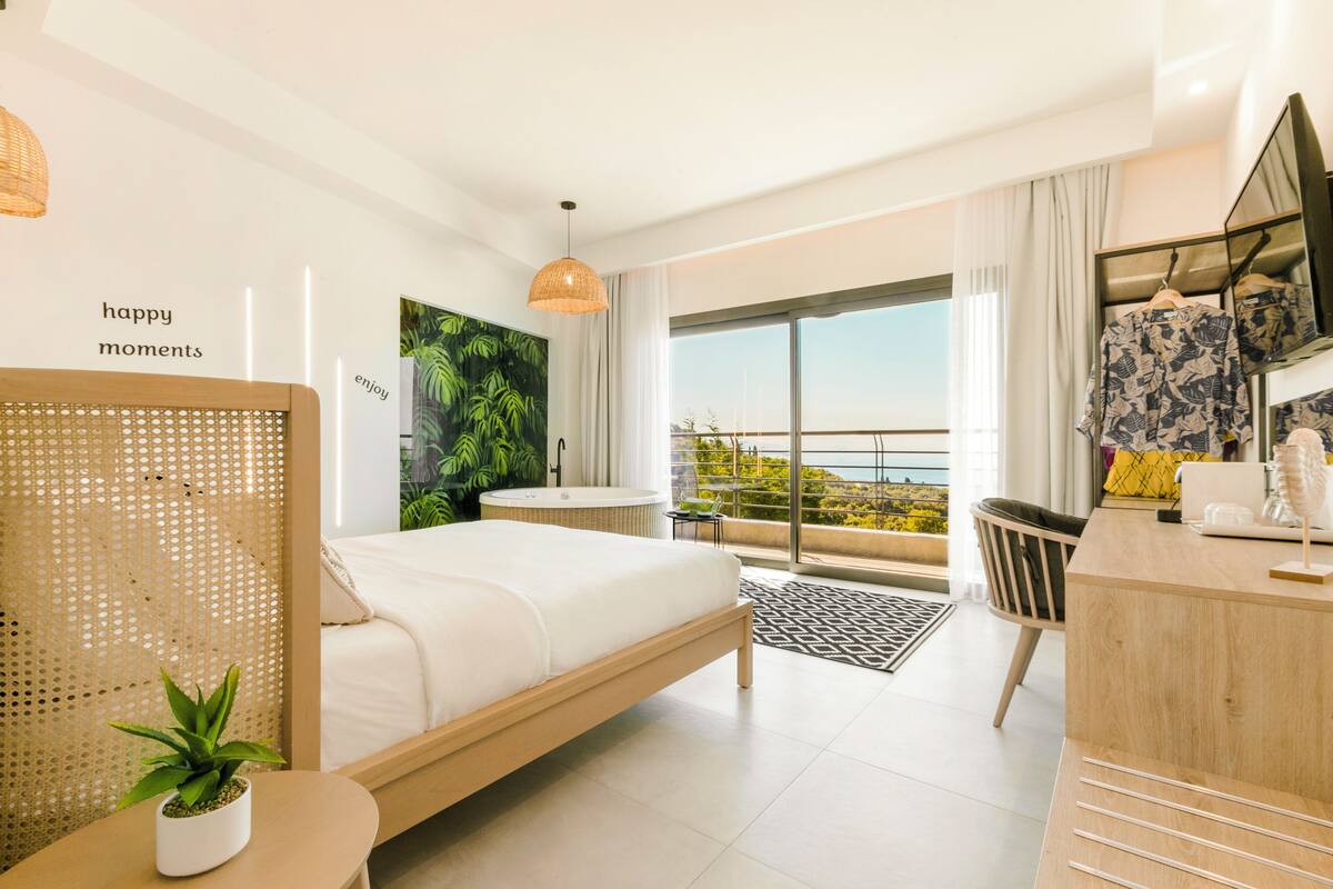 A modern hotel room with a bed, a desk, a bathroom, and a balcony with a view.