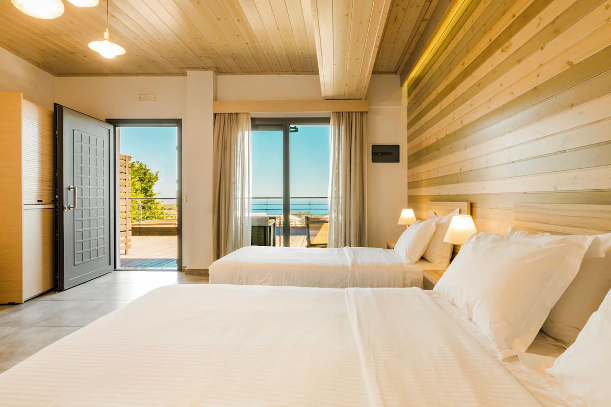 A hotel room with two beds, a balcony with a view, wooden ceiling, and a door leading outside.