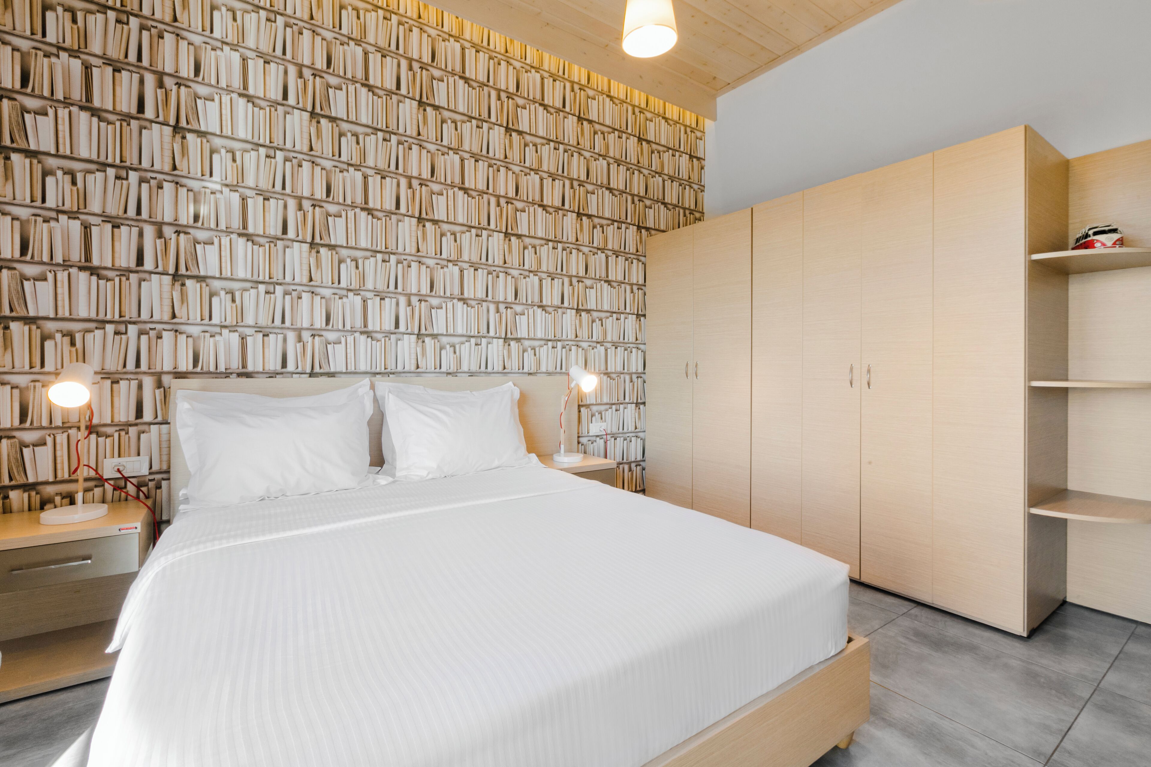 A bedroom with a large bed, a bookshelf wall, and a wooden wardrobe.