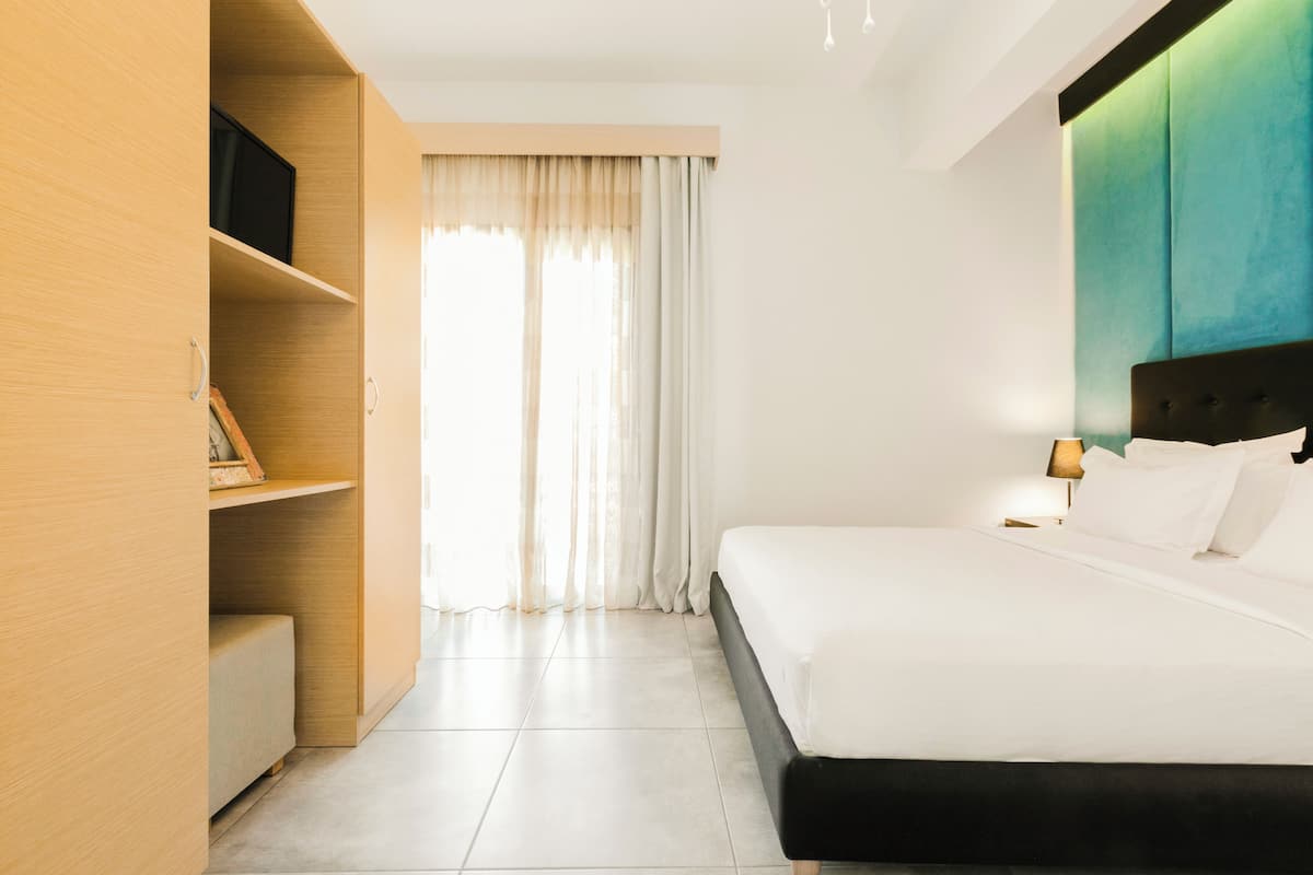 A modern hotel room with a large bed, wooden wardrobe, and a view of the outdoors through sheer curtains.