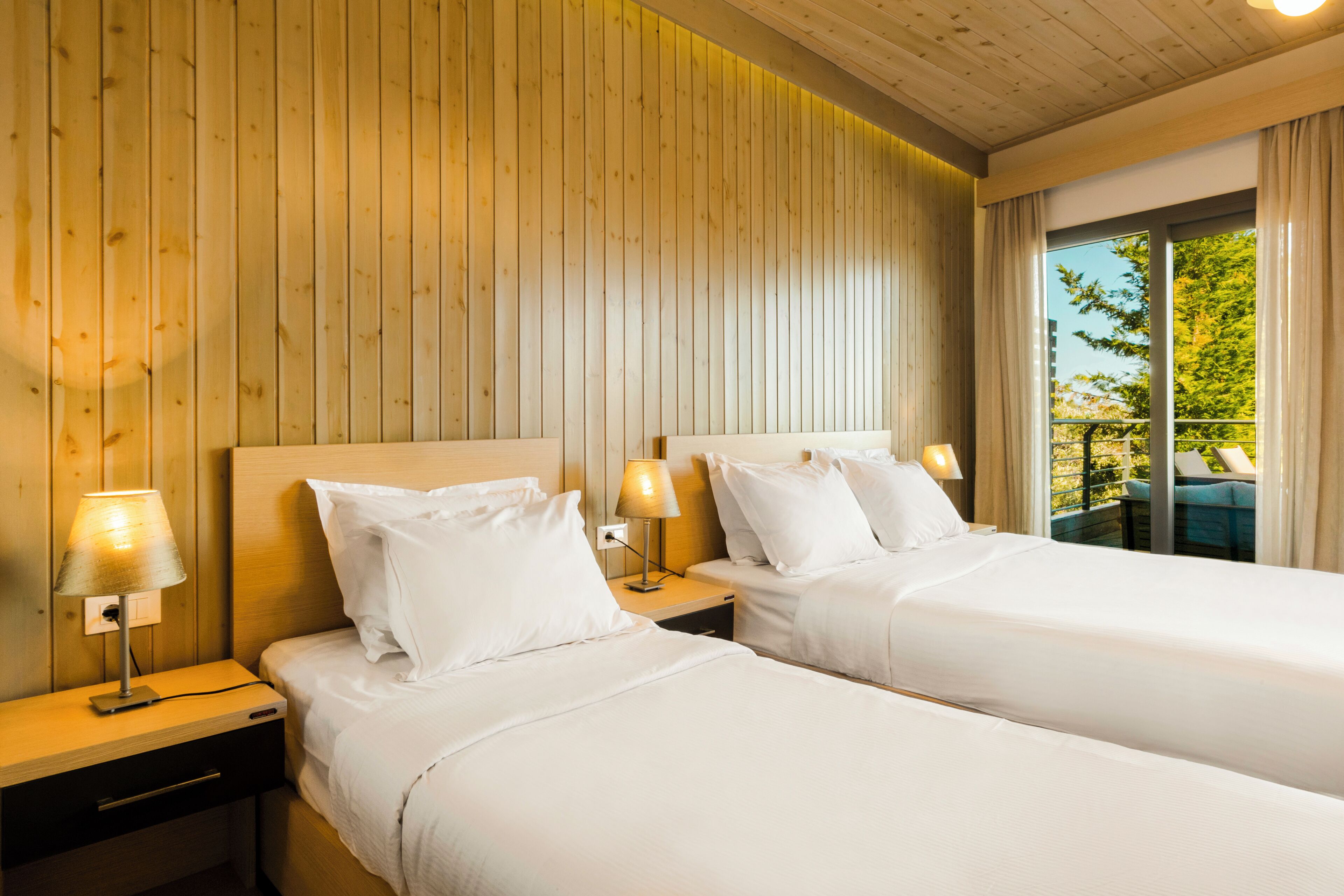 Een hotelkamer met twee bedden, wanden van houten panelen en een raam met gordijnen.