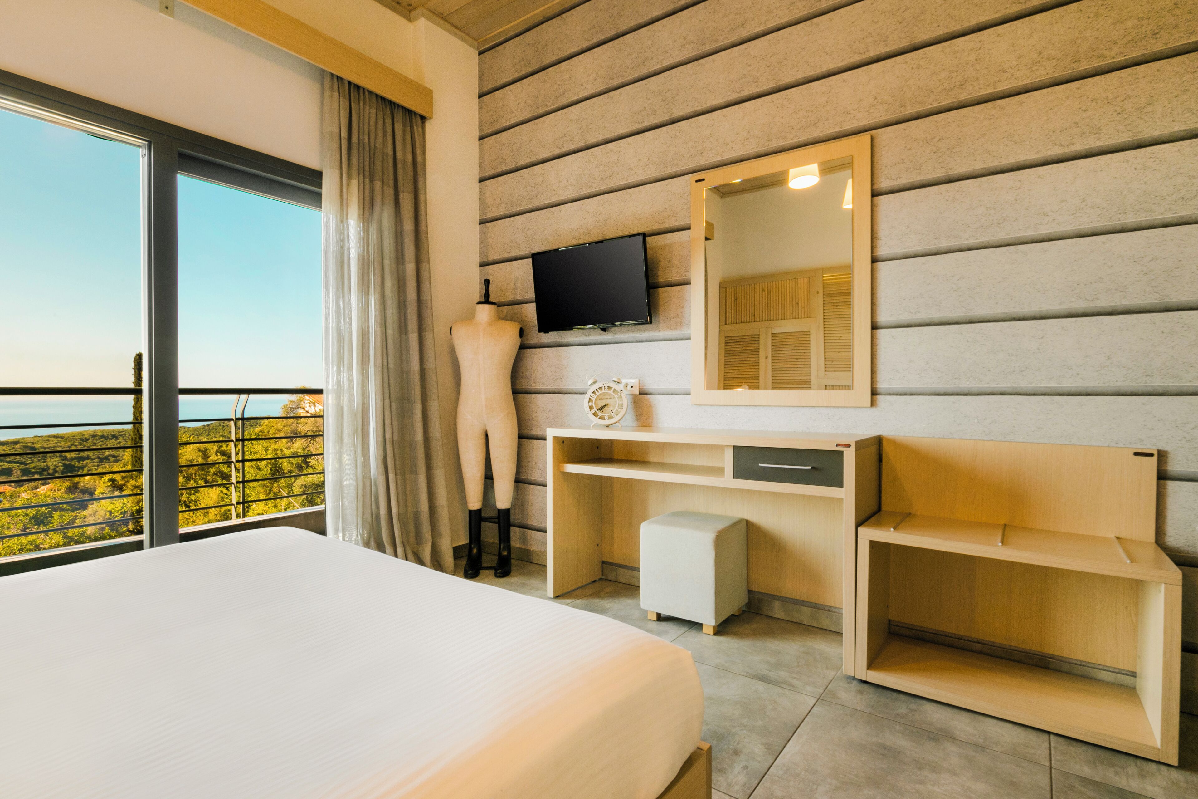 A hotel room with a large bed, a desk with a computer, a television, and a view of the outdoors.