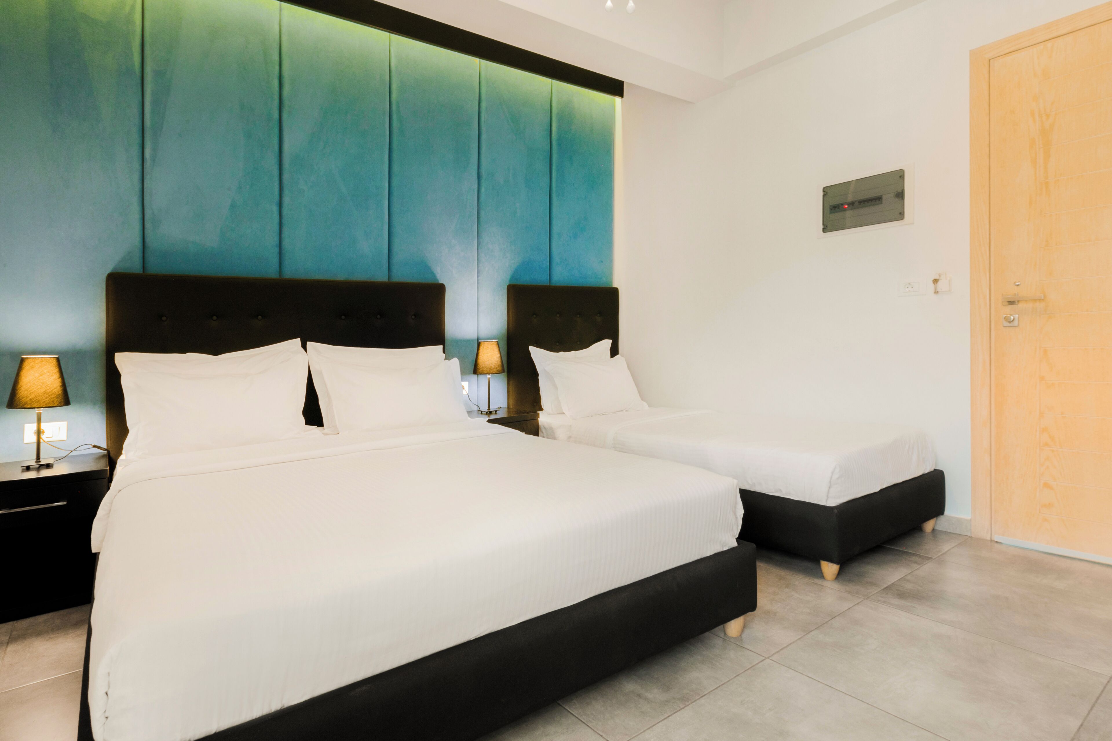 A hotel room with two beds, a wooden door, and a wall-mounted light fixture.