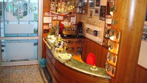 Una zona de bar con mostrador de madera, una máquina de café y estanterías con vasos y botellas.