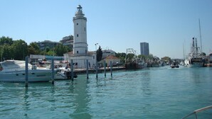 Un puerto deportivo con un faro blanco destacado, barcos amarrados y edificios al fondo.