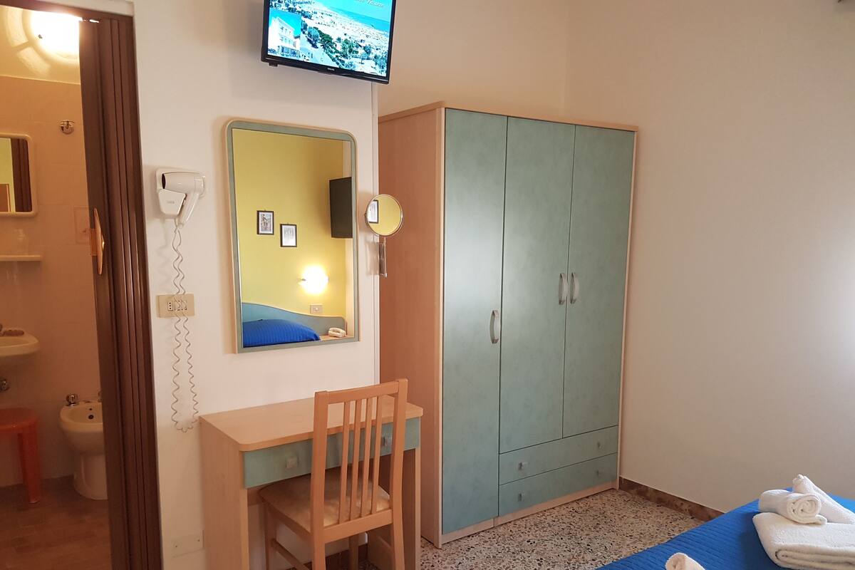 Une chambre à coucher comprenant un lit, un bureau, une chaise, une armoire, un miroir et un téléviseur.