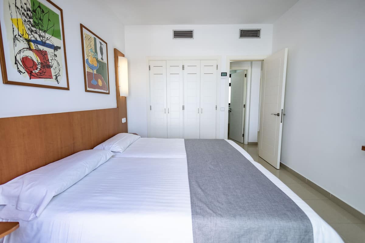 Een hotelkamer met een groot bed, een houten hoofdbord, twee ingelijste kunstwerken aan de muur en een aantal witte kasten.