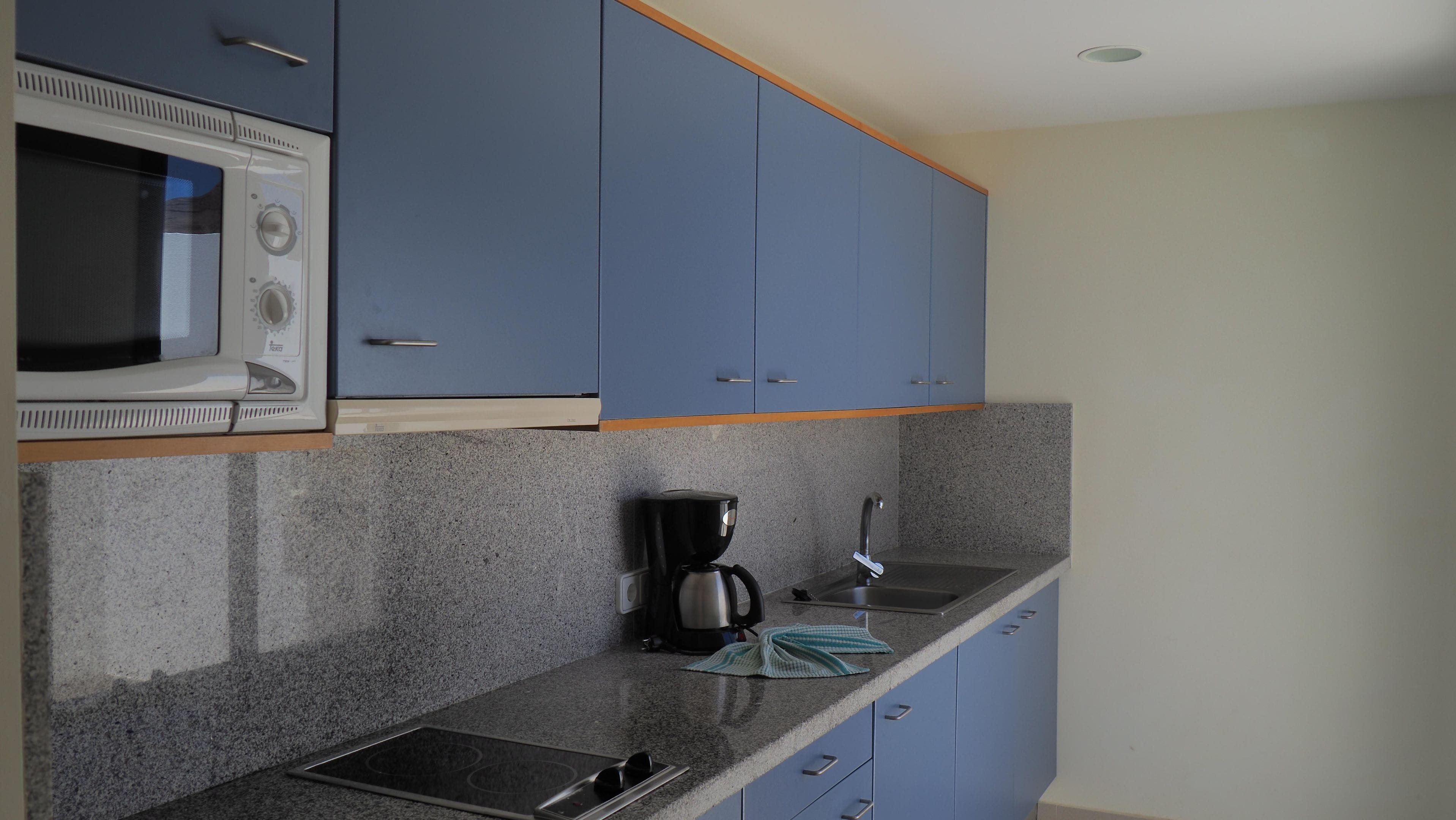 A kitchen with blue cabinets, a microwave, a coffee maker, and granite countertops.
