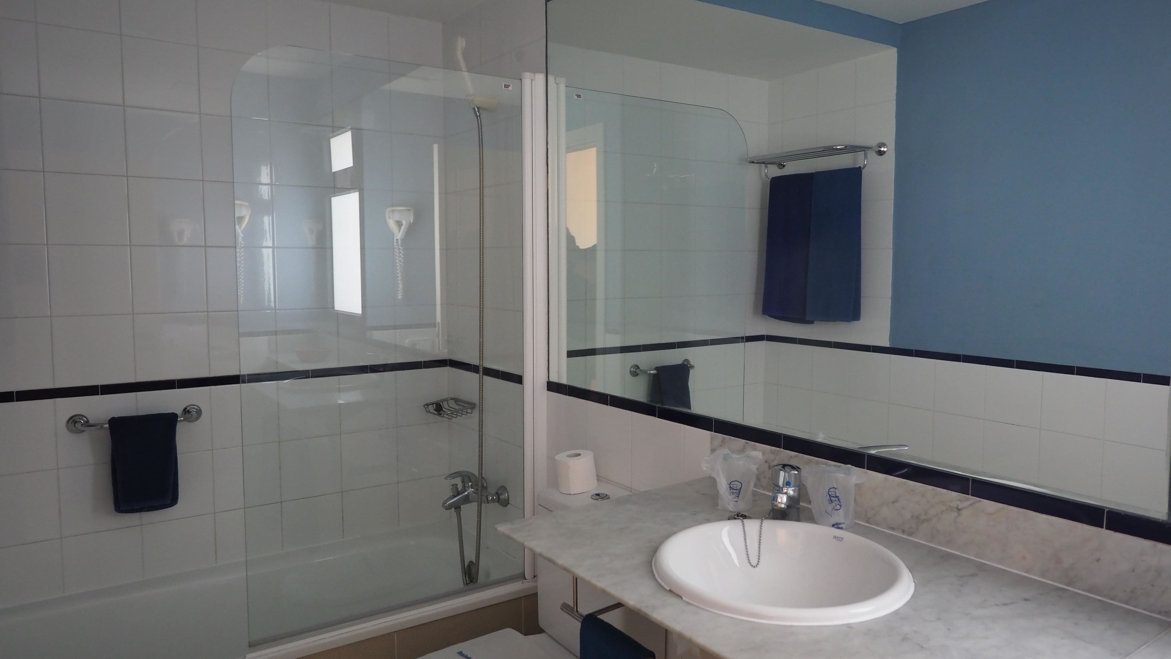 Un baño con ducha envuelta en vidrio, un lavabo blanco y un espejo grande.