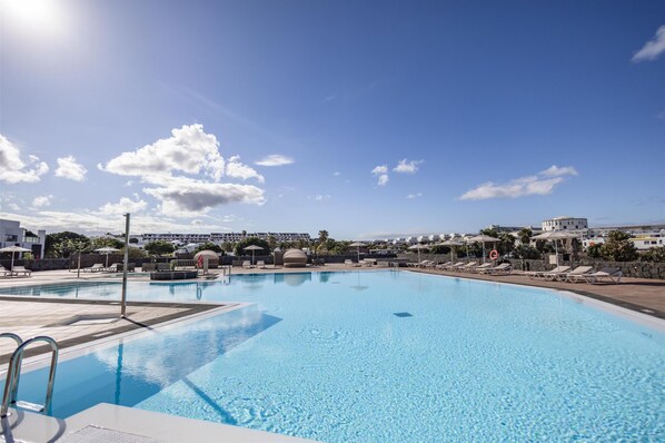 Una piscina al aire libre, sombrillas, sillones reclinables de piscina