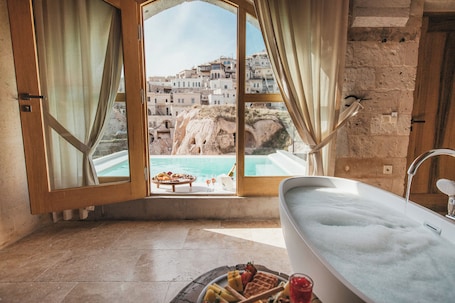 A bathroom with a bathtub, a view of a pool, and a breakfast setup.