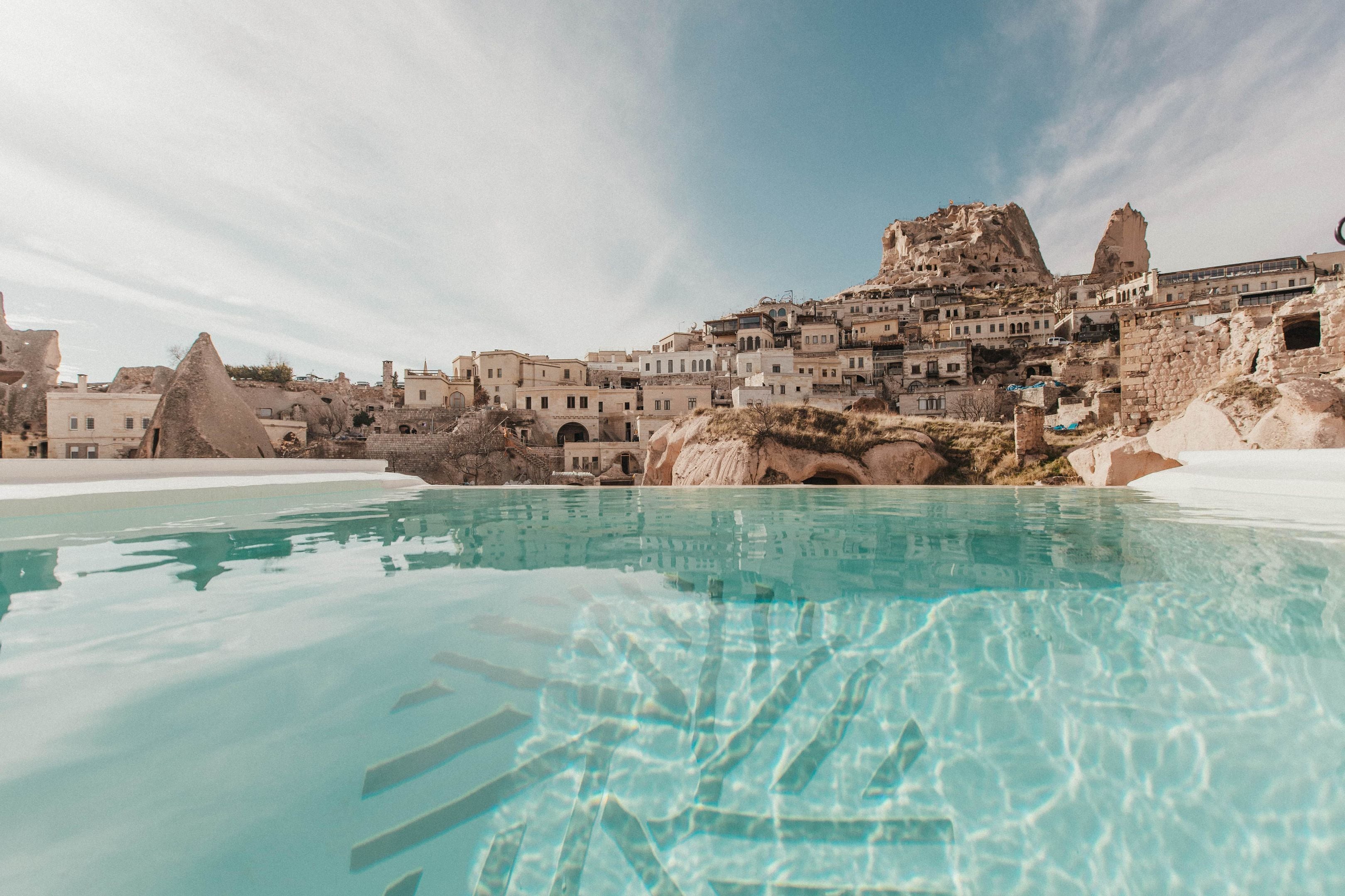 A pool with clear water, surrounded by buildings with unique rock formations and a mountainous backdrop.
