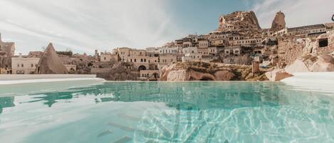 A pool with clear water, surrounded by buildings with unique rock formations and a mountainous backdrop.