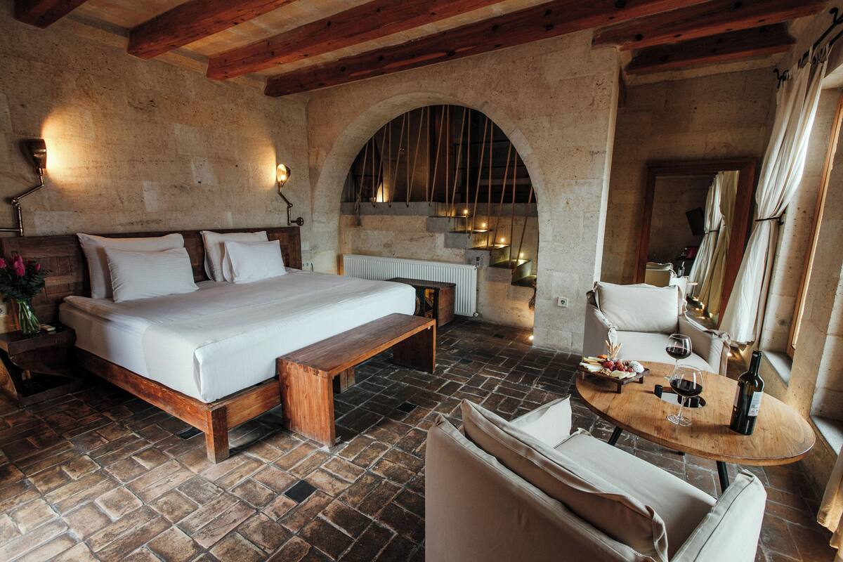 A bedroom with a wooden bed, a bench, a small table with a bottle and glass, and a mirror.