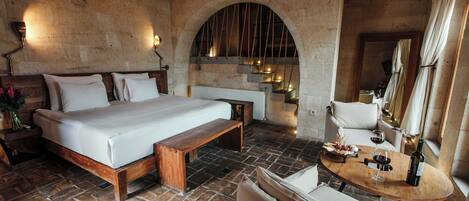 A bedroom with a wooden bed, a bench, a small table with a bottle and glass, and a mirror.