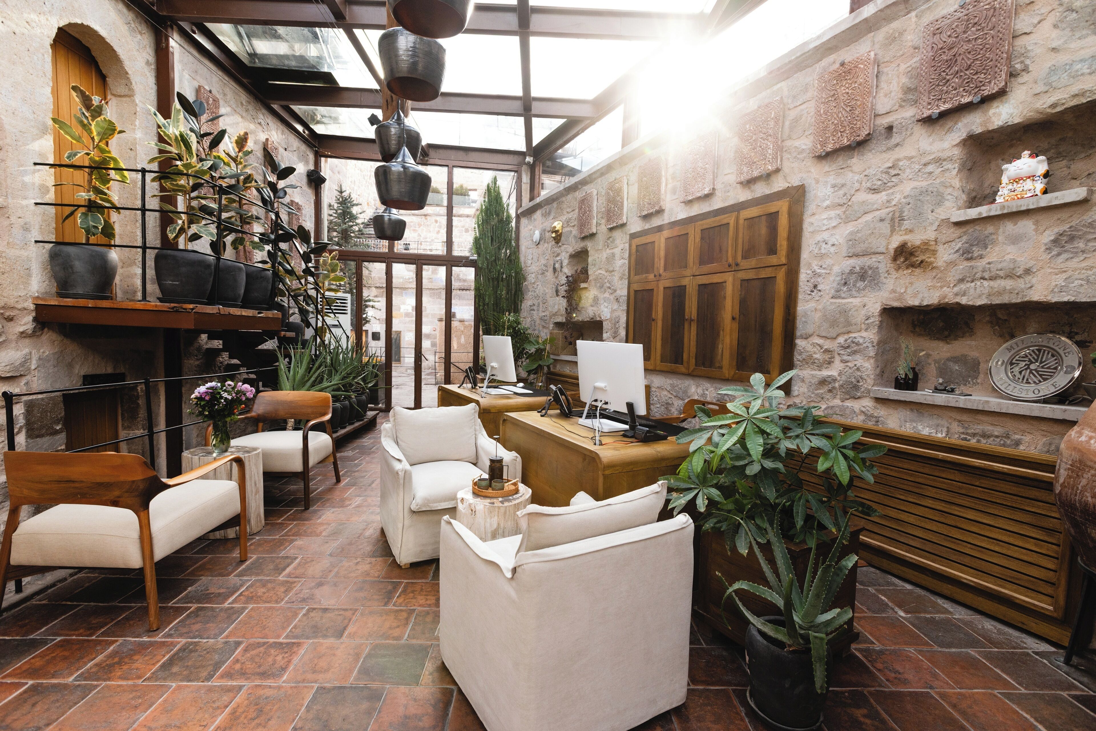 A cozy indoor seating area with a wooden reception desk, comfortable chairs, and various potted plants.