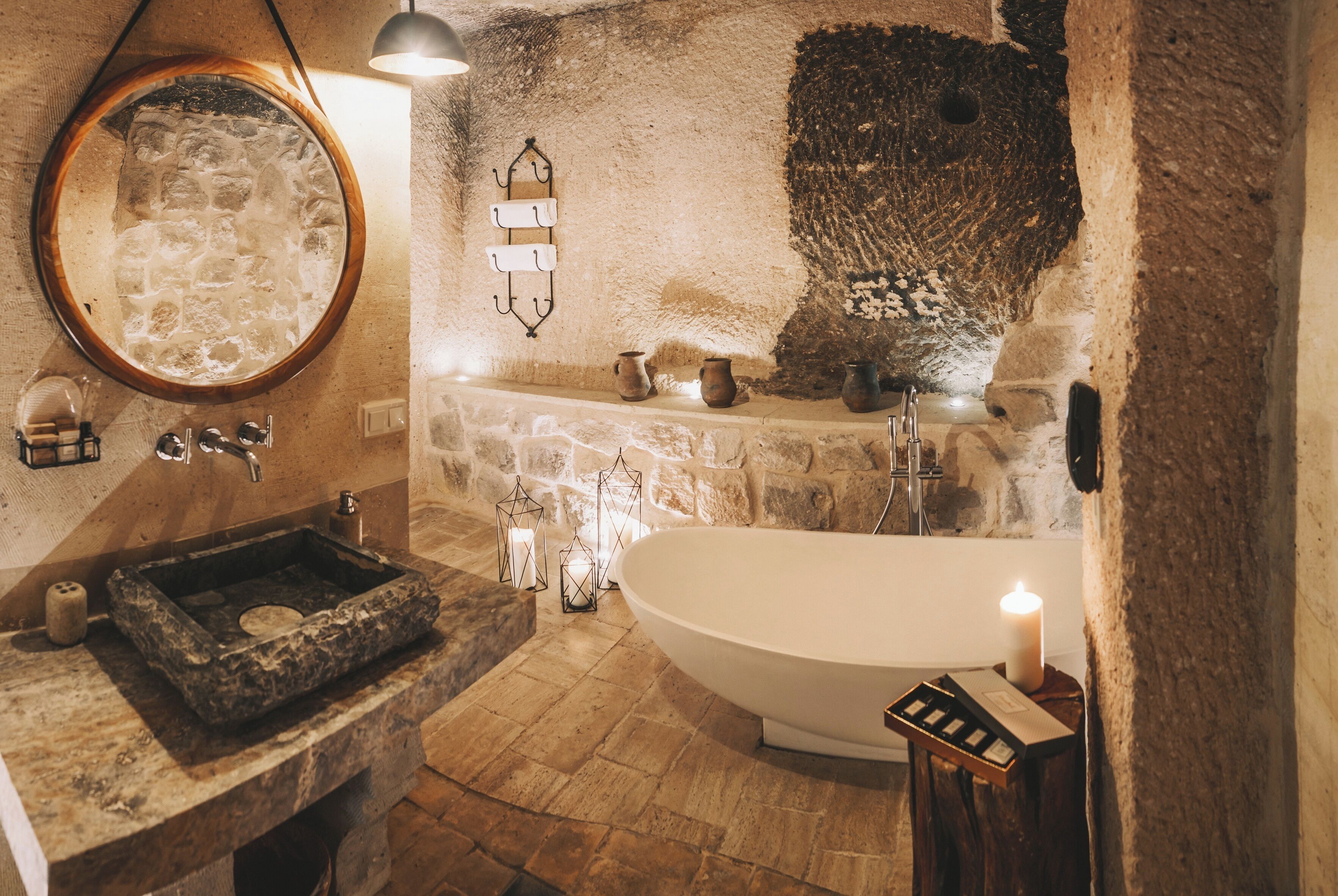 A rustic bathroom with a stone sink, a freestanding bathtub, and a mirror with a wooden frame.