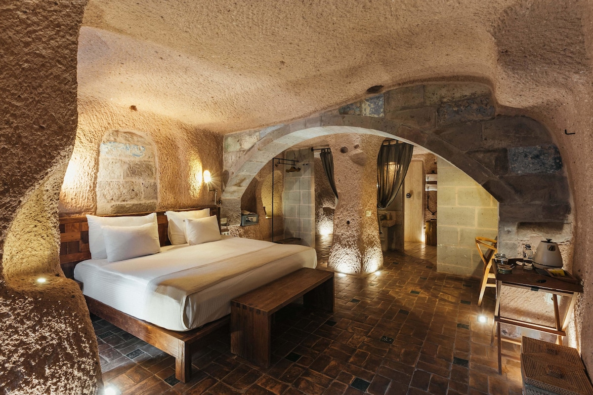 A rustic bedroom with a large bed, wooden bench, and a stone archway.
