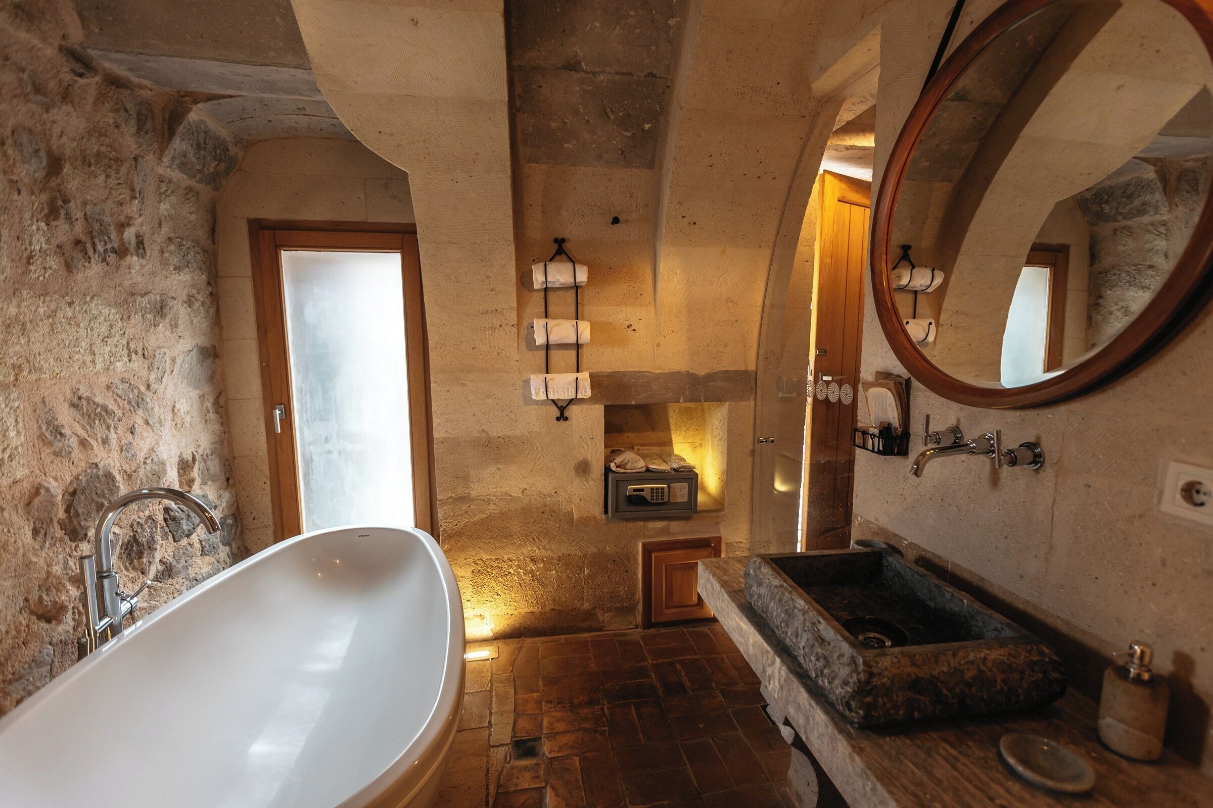 A rustic bathroom with a freestanding bathtub, a stone sink, and a mirror.