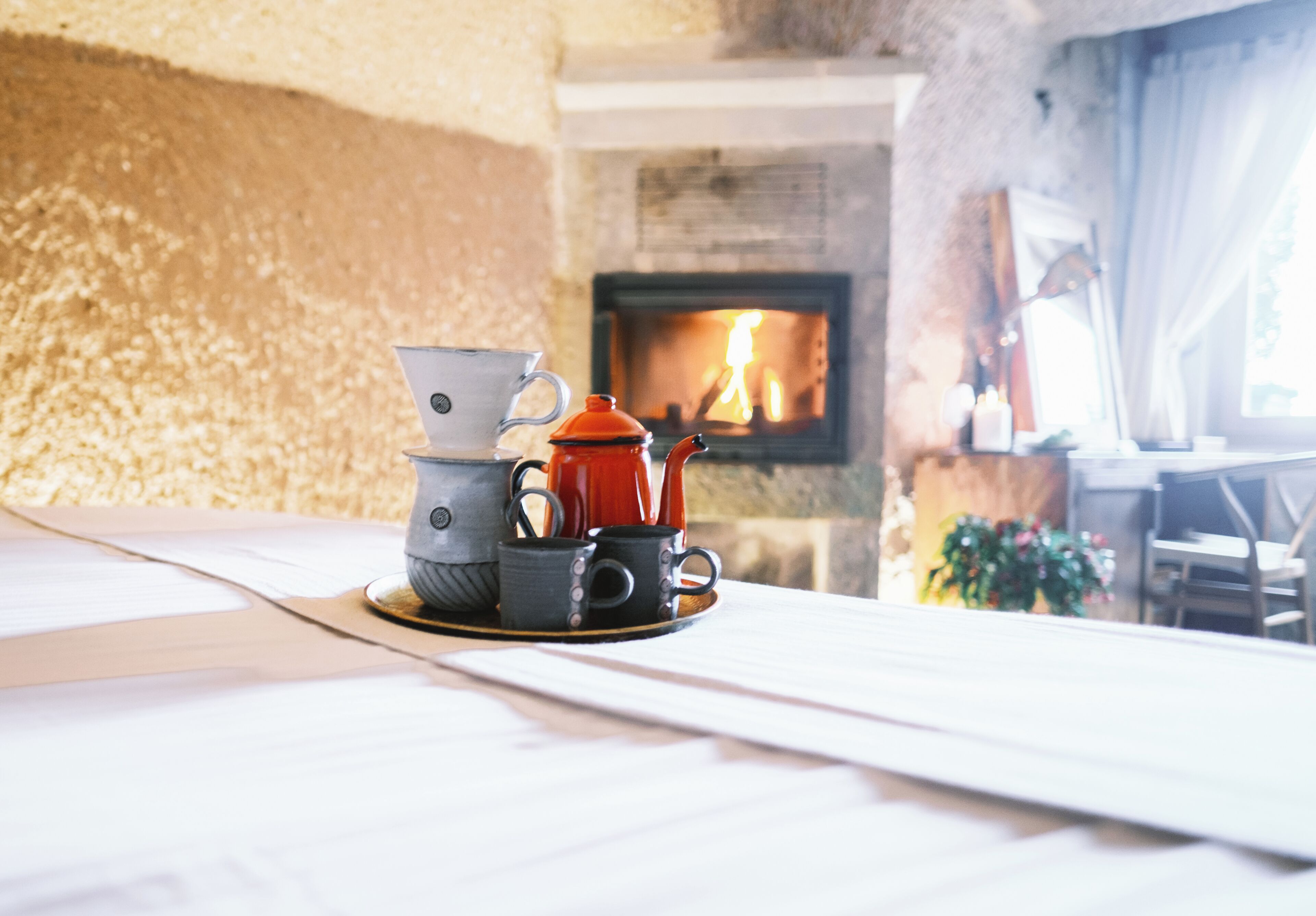 A cozy room with a fireplace, a table with a tea set, and a view of the fire.