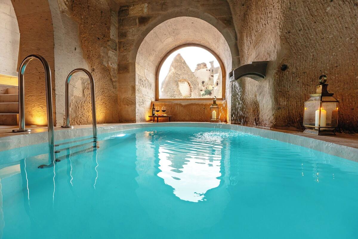 A pool with clear water, stone walls, and a view of buildings through an arched window.