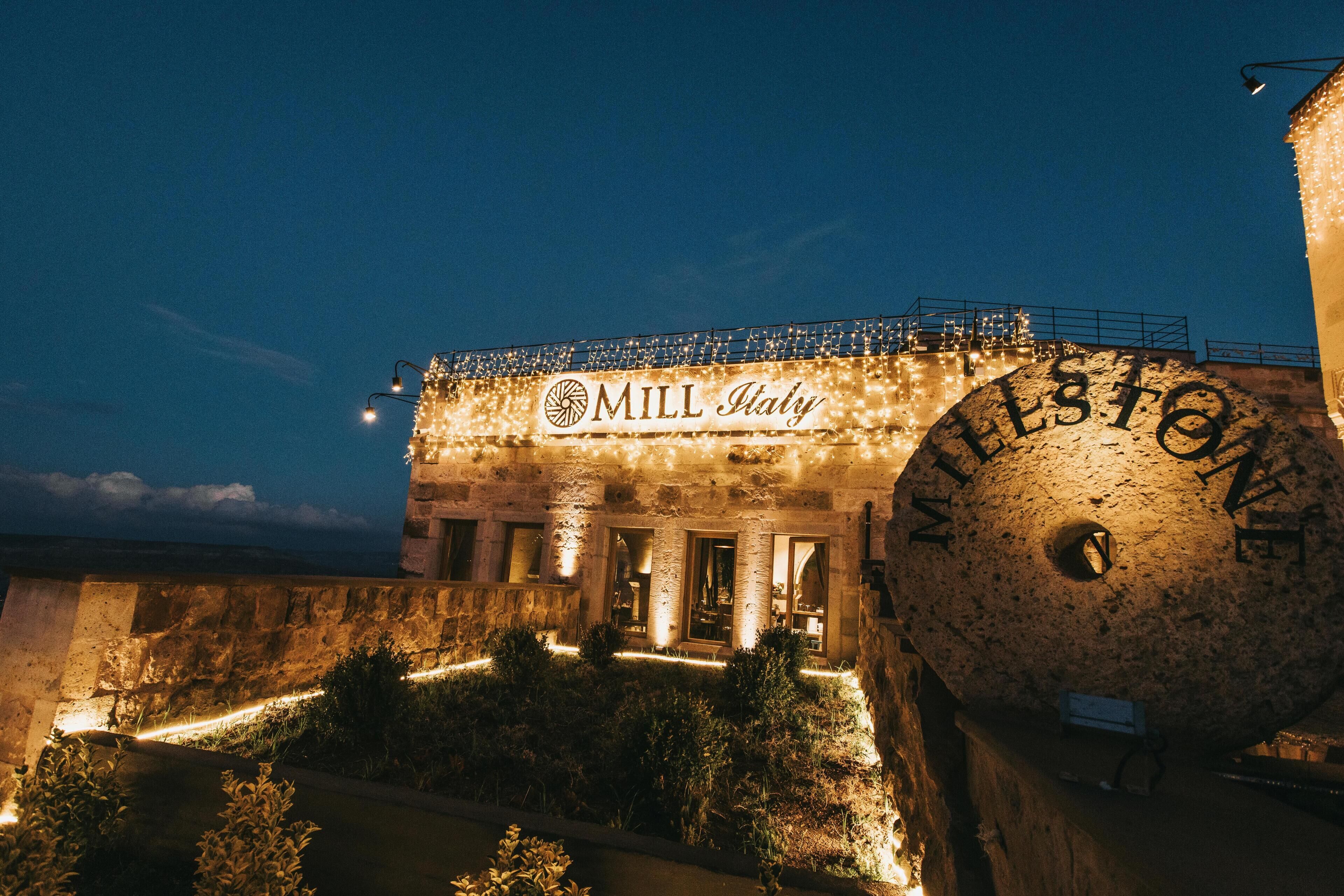 A building with the sign "MILL Italy" and "MELESTONE" on its facade, featuring stone architecture and outdoor lighting.
