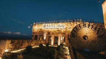 A building with the sign "MILL Italy" and "MELESTONE" on its facade, featuring stone architecture and outdoor lighting.