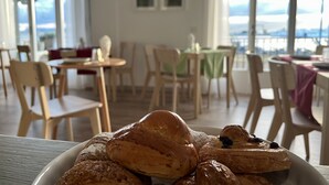 En matplats med bord och stolar, en tallrik med bakverk i förgrunden och en utsikt genom stora fönster.