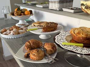 Un bufé de desayuno con diversas opciones de pastelería, incluyendo cruasanes y un pastel, sobre una mesa de madera.
