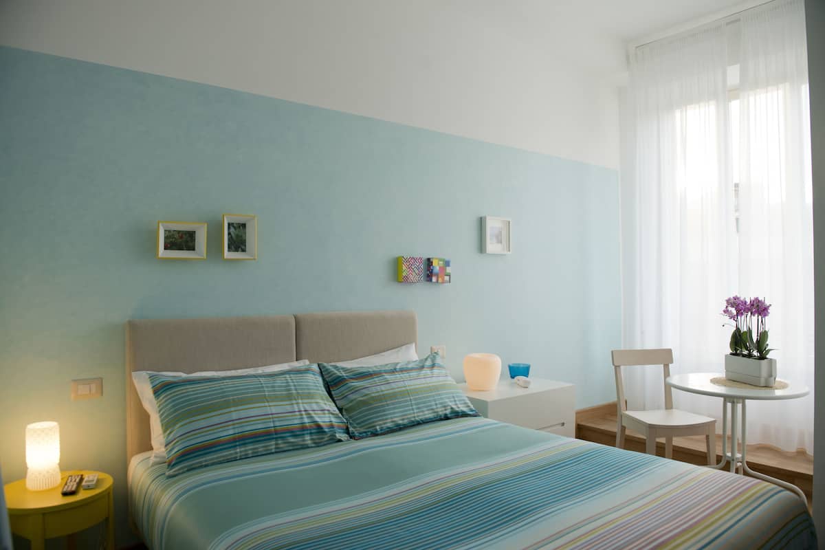 A hotel room with a bed, a nightstand, a chair, and a small table with a plant.