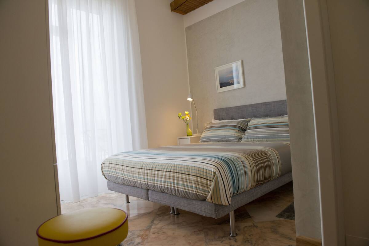 A bedroom with a bed, a bedside table, a lamp, and a window with curtains.