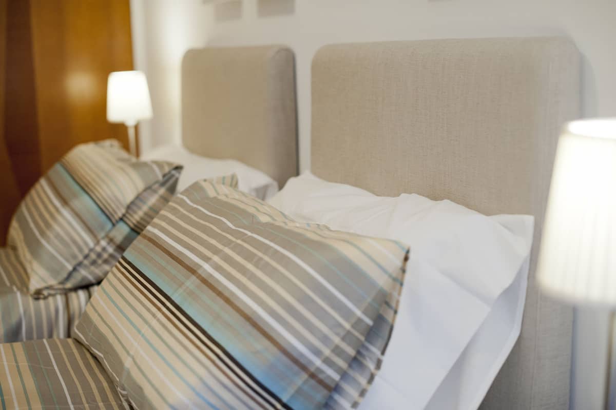 A hotel room with a bed, striped pillows, and a bedside lamp.