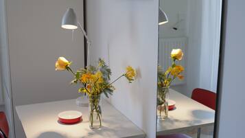 Ein Tisch mit einer Blumenvase, einem roten Teller, einer Lampe und einem roten Stuhl.