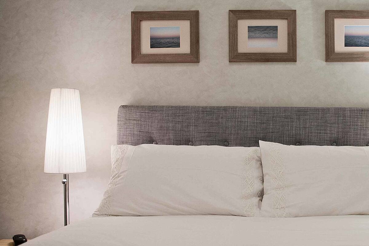A neatly made bed with white linens, a grey headboard, and three framed pictures on the wall.
