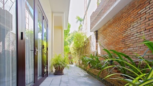 A narrow pathway with a brick wall on one side and glass doors on the other. There are potted plants along the path. - Pham Gia Boutique Villa (Da Nang)