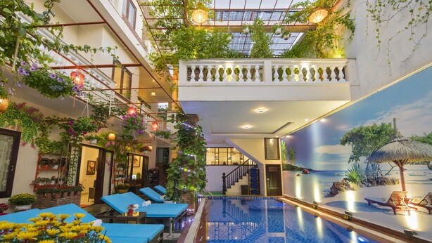 An indoor swimming pool with a tropical mural, lounge chairs, and potted plants. - Pham Gia Boutique Villa (Da Nang)