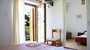 A bedroom with a bed, a chair, a TV, and a door leading to a balcony. - Hotel Artemon (Sifnos)