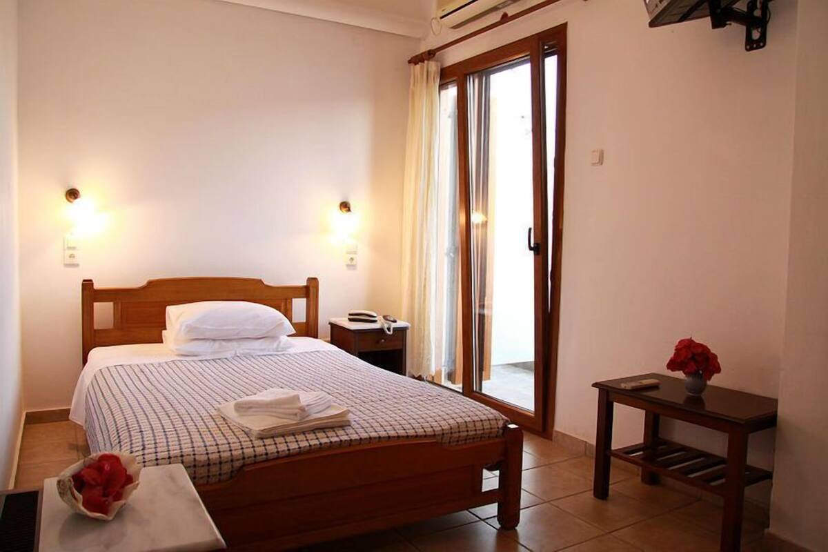 A neatly made bed with a checkered bedspread, a bedside table with a lamp, and a small table with a vase of flowers.