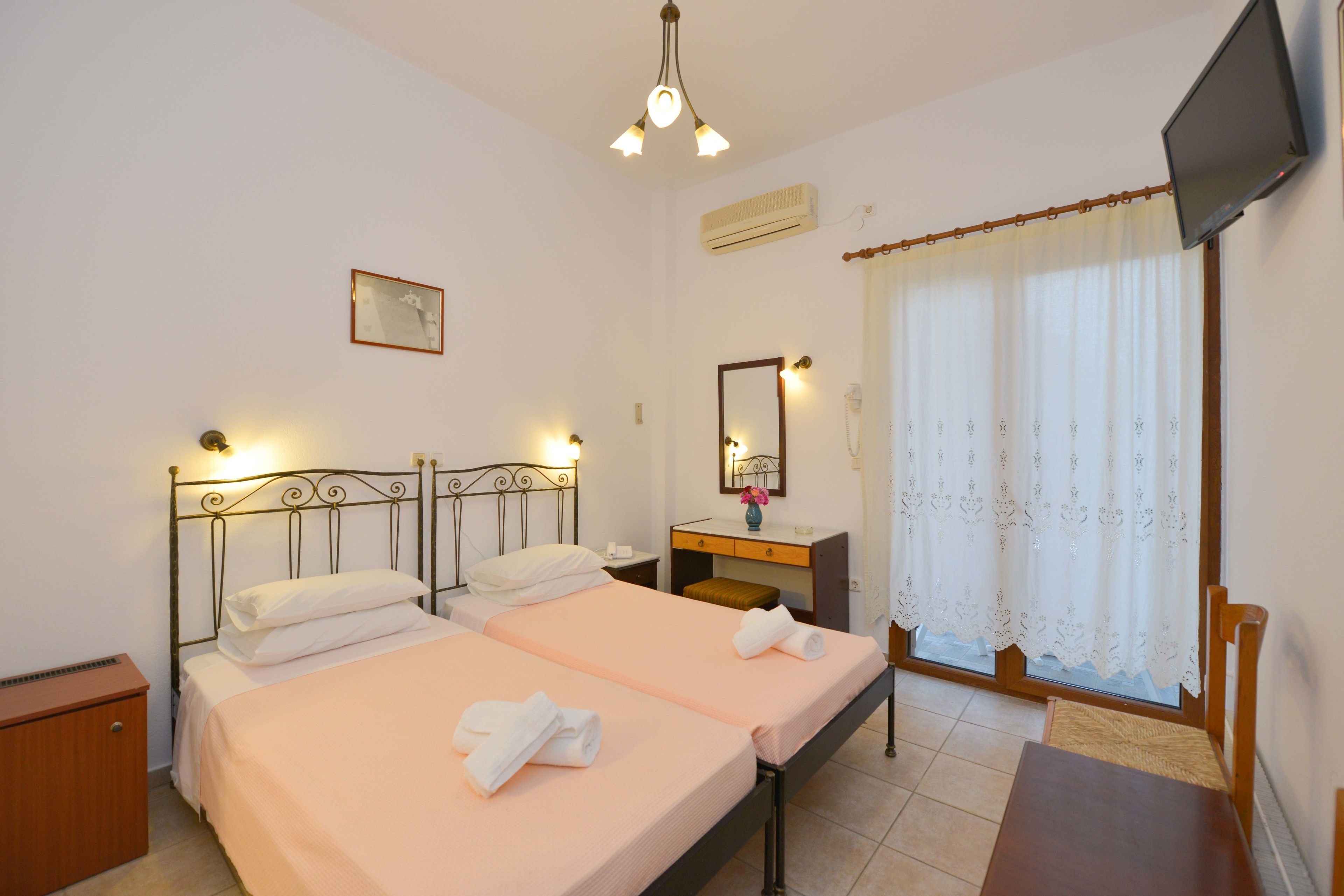 Habitación de hotel con dos camas, televisión, ventana con cortinas y una mesita.