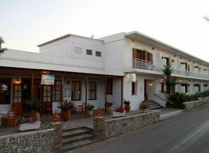 A two-story building with a white facade, a balcony on the upper floor, and a stone wall in front. - Hotel Artemon (Sifnos)