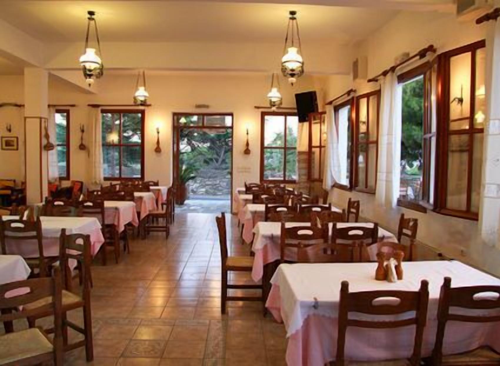 Un espace repas avec des tables dressées pour les convives, de grandes fenêtres et des luminaires suspendus.