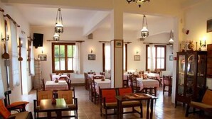 A dining area with multiple tables and chairs, wooden floors, and hanging light fixtures. - Hotel Artemon (Sifnos)