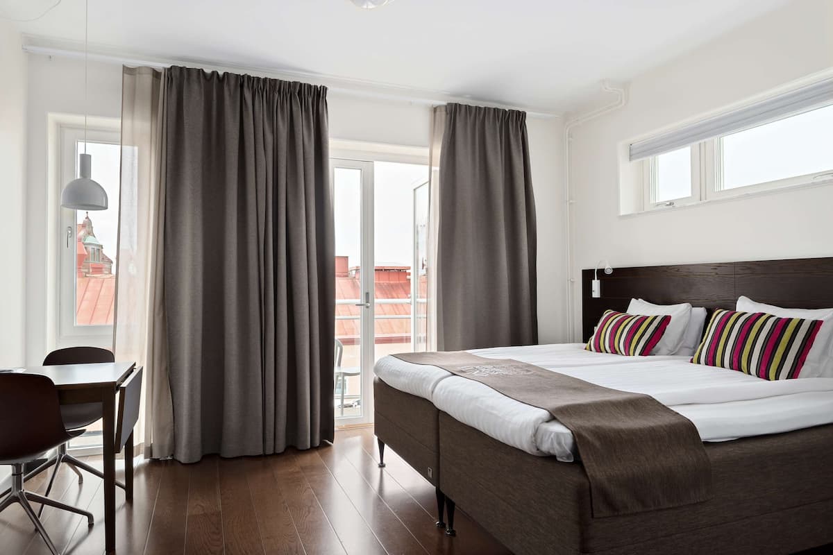Quarto de hotel com cama, escrivaninha e vista para um edifício pela janela.